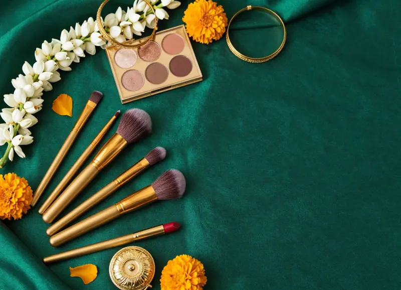 Flat lay of makeup, gold brushes and jasmine on emerald silk