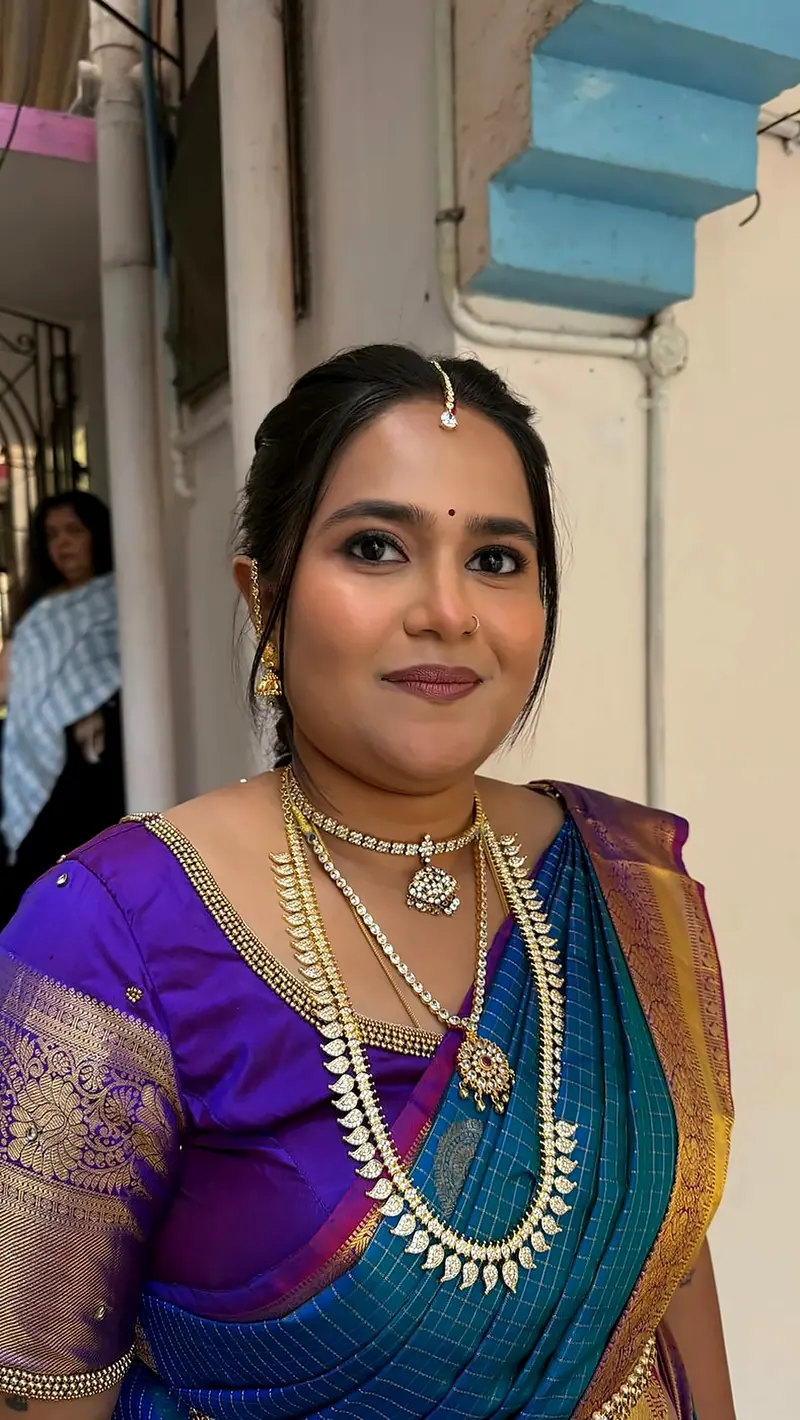 Woman in a purple and teal silk saree with gold necklaces