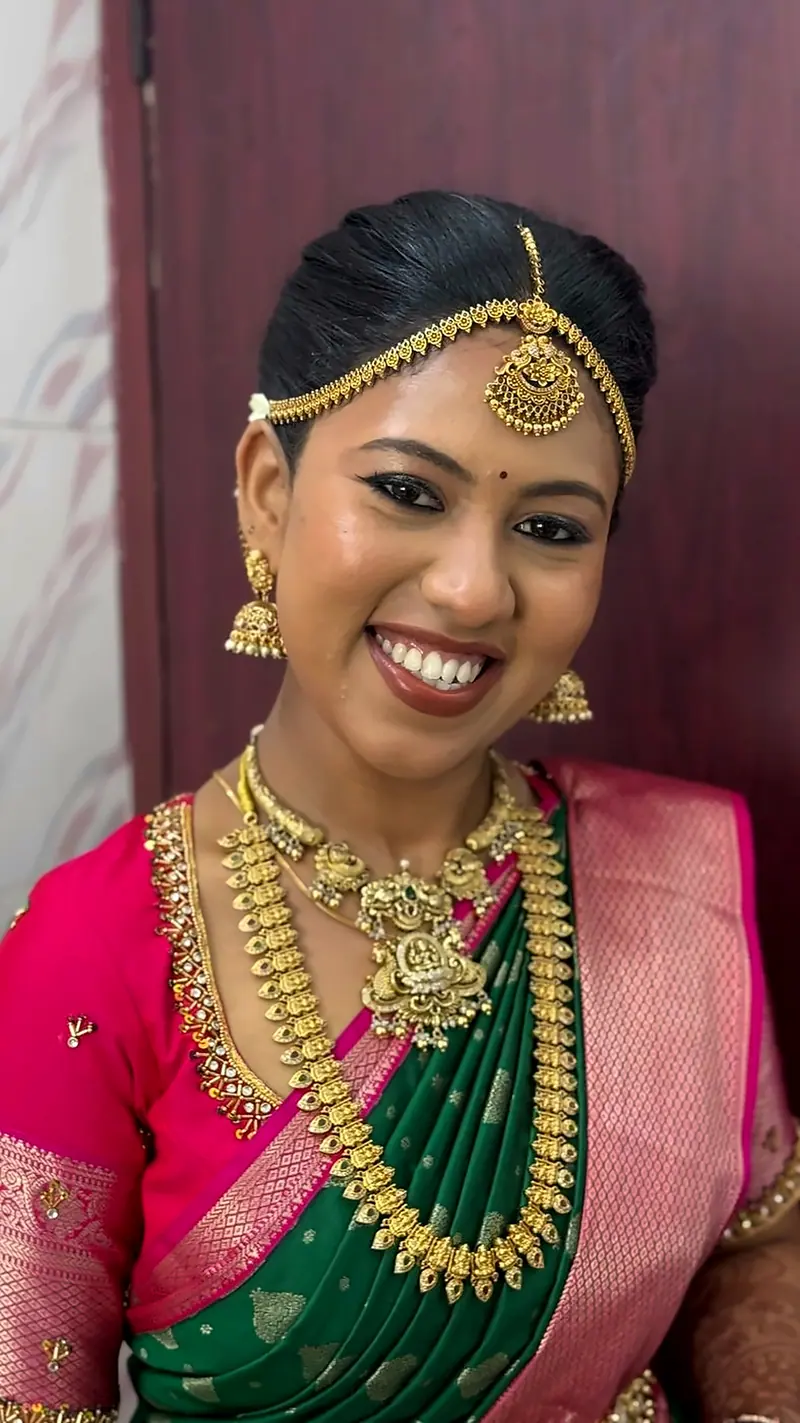 Bride in pink silk saree with a green pallu and gold necklace