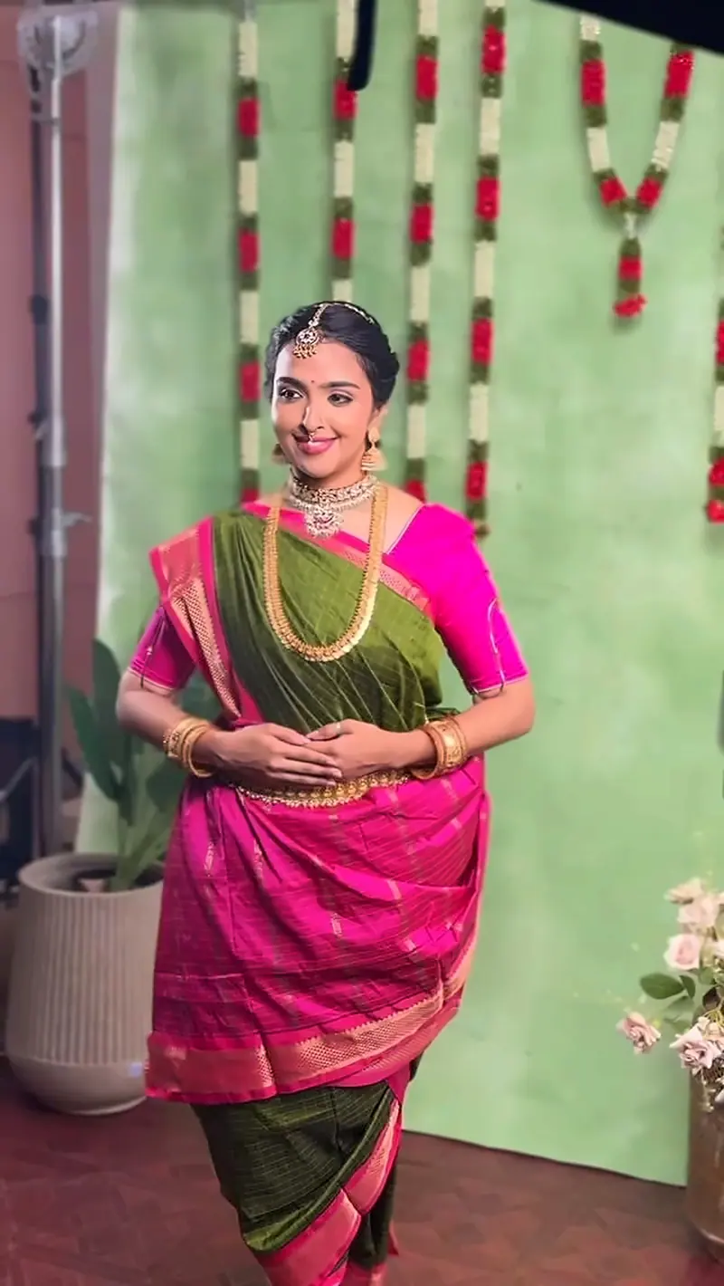 Woman in a pink and green silk saree in front of a flower-garland backdrop