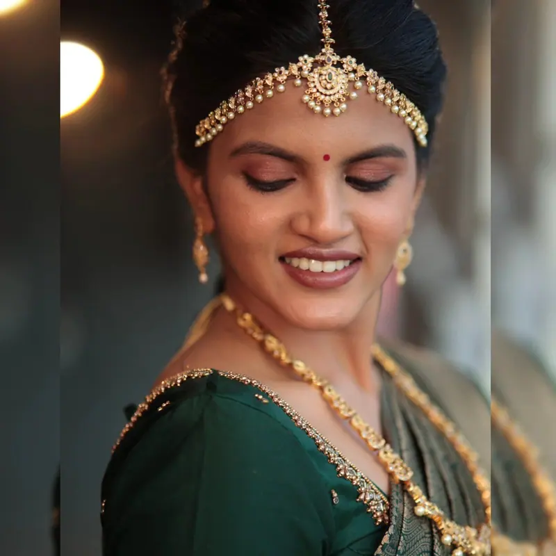 Bride with a maang tikka and a soft downward gaze, bridal makeup by Kamali Artistry