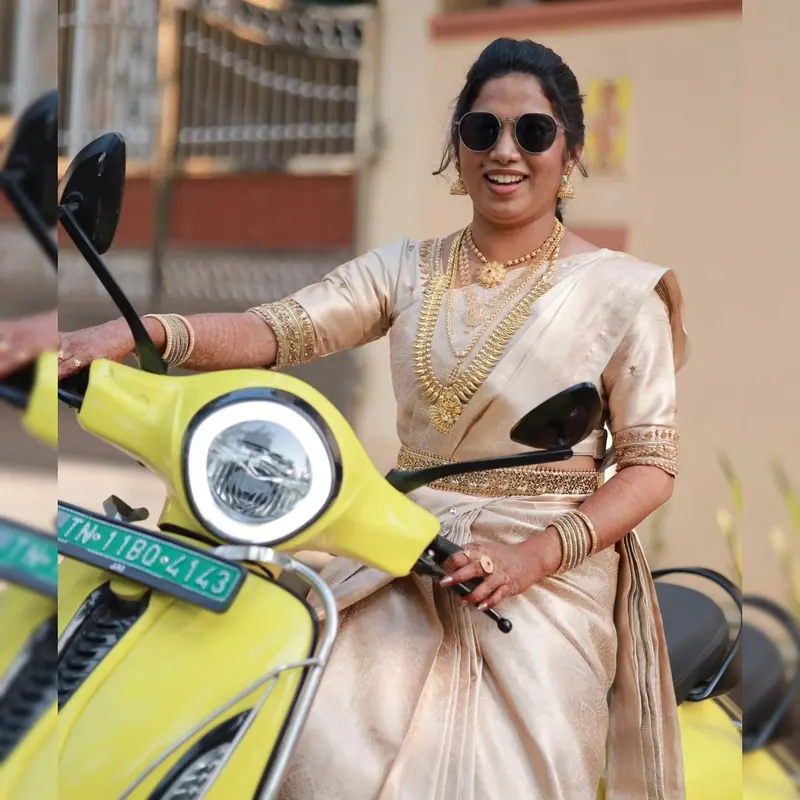 Woman in a cream saree riding a yellow scooter, neatly draped